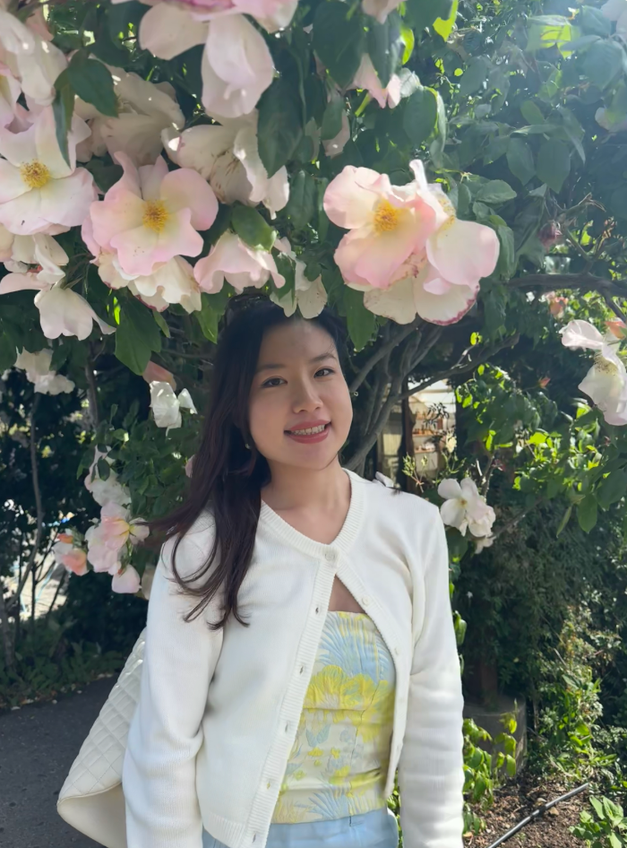 Angela Xie, smiling beneath a pink flowering tree